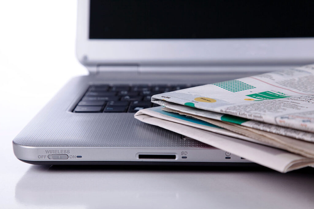 Pila de periódicos sobre un ordenador portátil que indica la publicación de actos corporativos